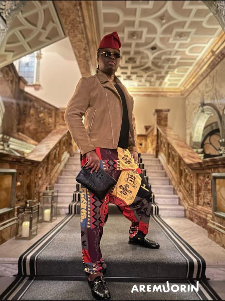 Aremuorin wearing a red hat and brown suede jacket, holding a crocodile clutch on a grand staircase